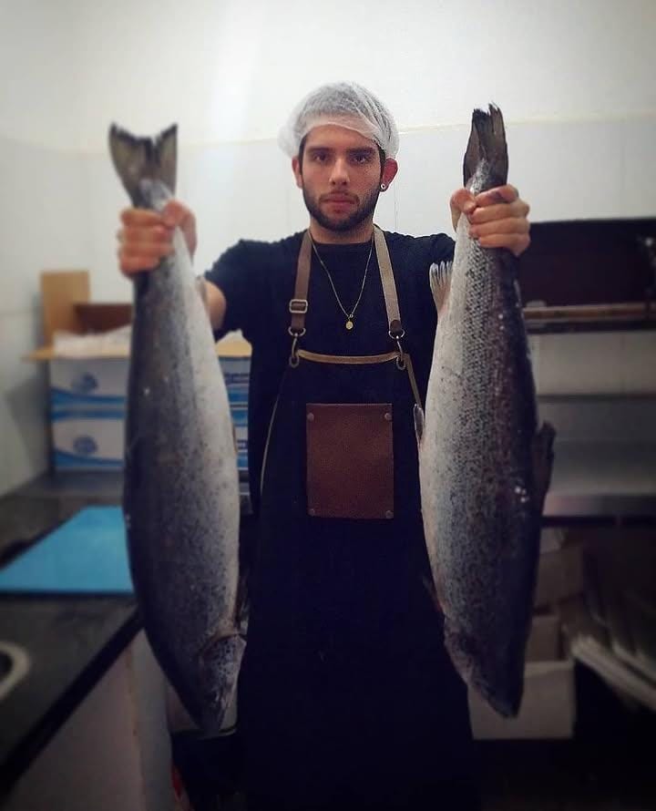 Guilherme holding two salmon in the kitchen